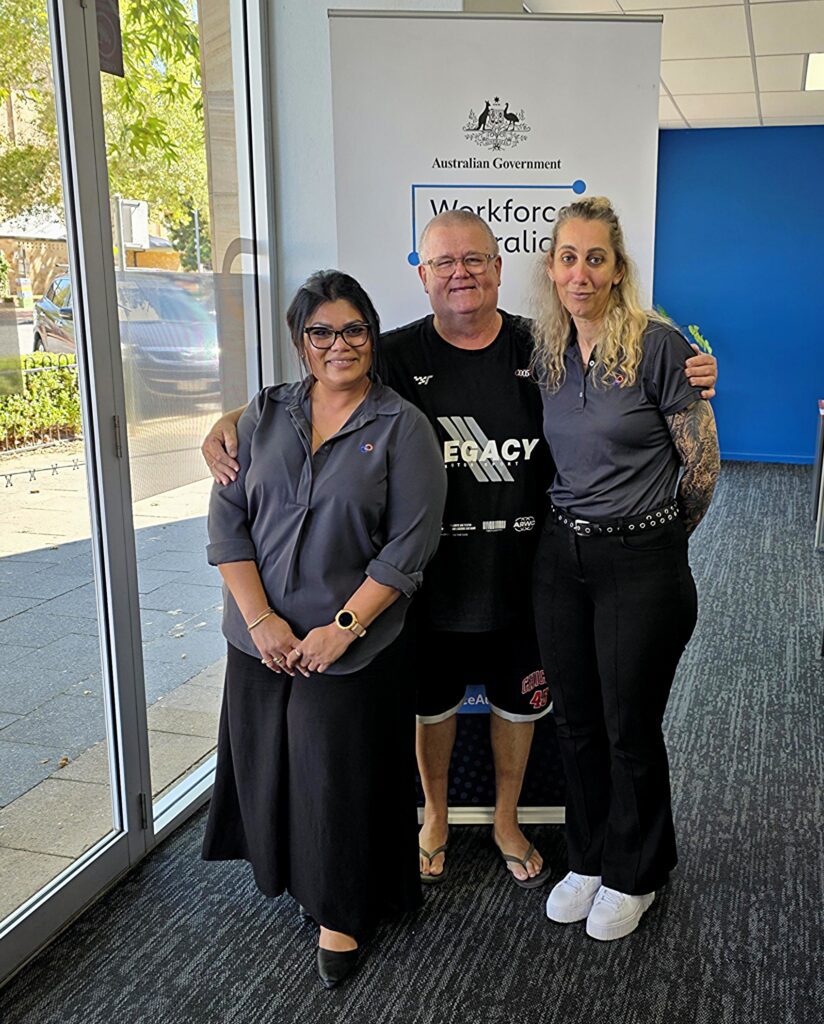 Over 55 jobseeker with female work support mentors in office in front of sign.
